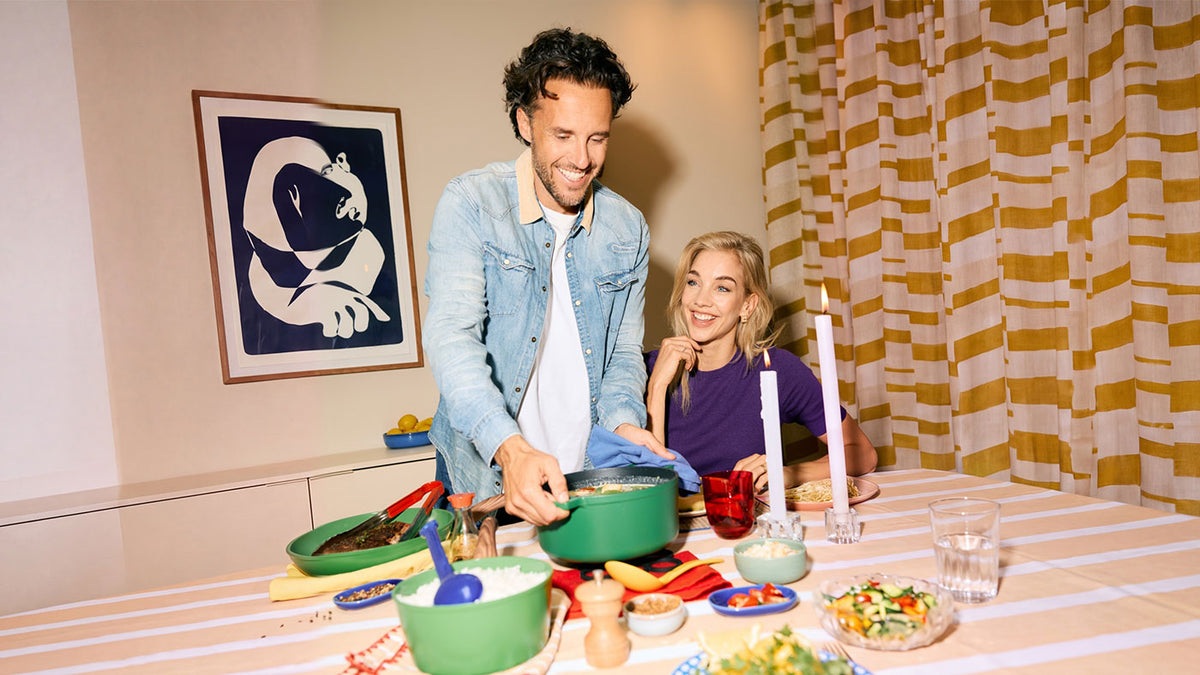 Man serveert uit een groene gietijzeren braadpan aan tafel