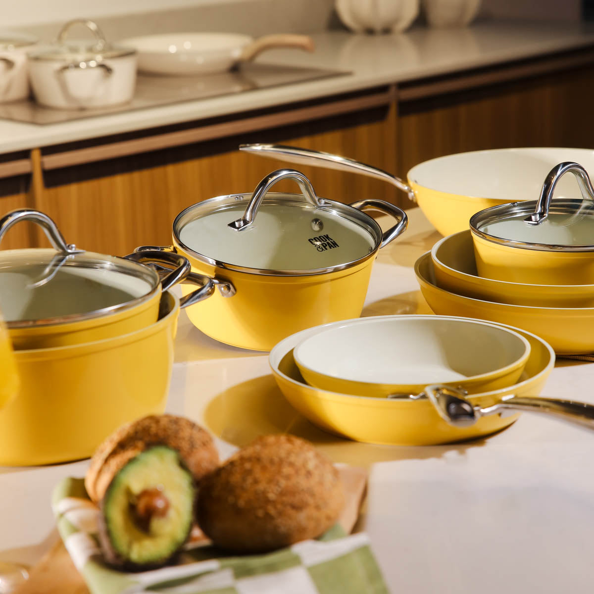 Batterie de cuisine jaune 9 pièces avec couvercles en verre et poignées en acier inoxydable sur plan de travail.