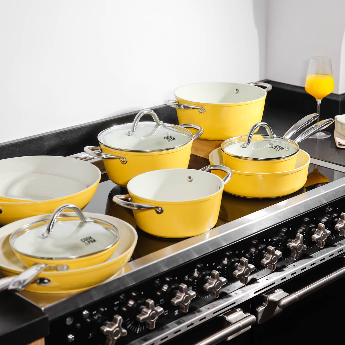 Yellow 9-piece cookware set with glass lids and white interior on black stove.