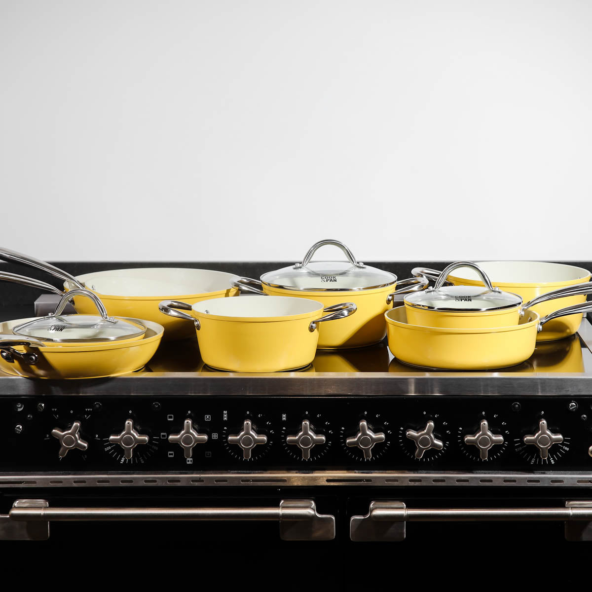 Yellow ceramic 9-piece cookware set with stainless steel handles and glass lids on a black stove top.
