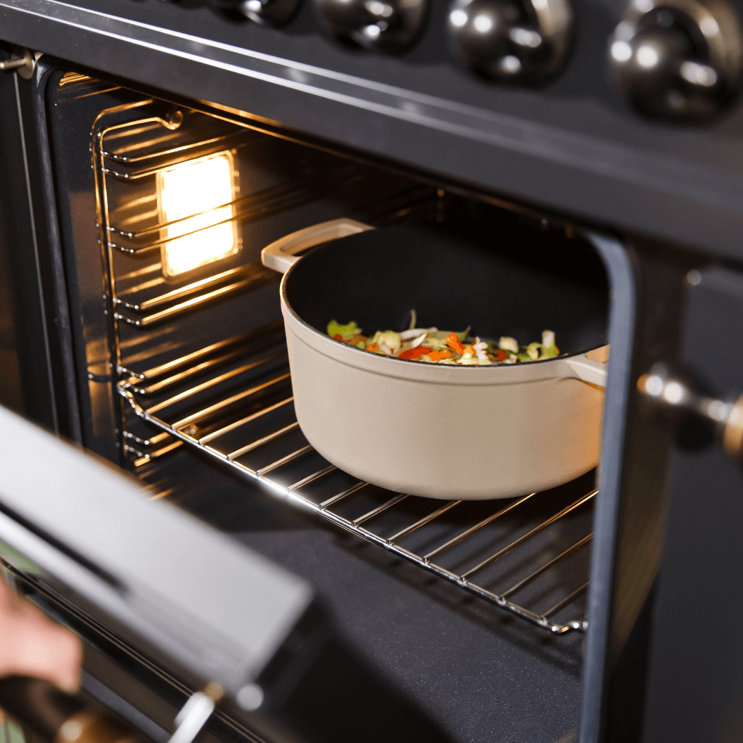 Cocotte en fonte taupe avec couvercle, remplie de légumes, placée dans un four sur une grille métallique.