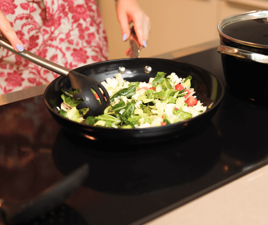 Zwarte koekenpan met groenten op zwarte inductiekookplaat in moderne keuken.