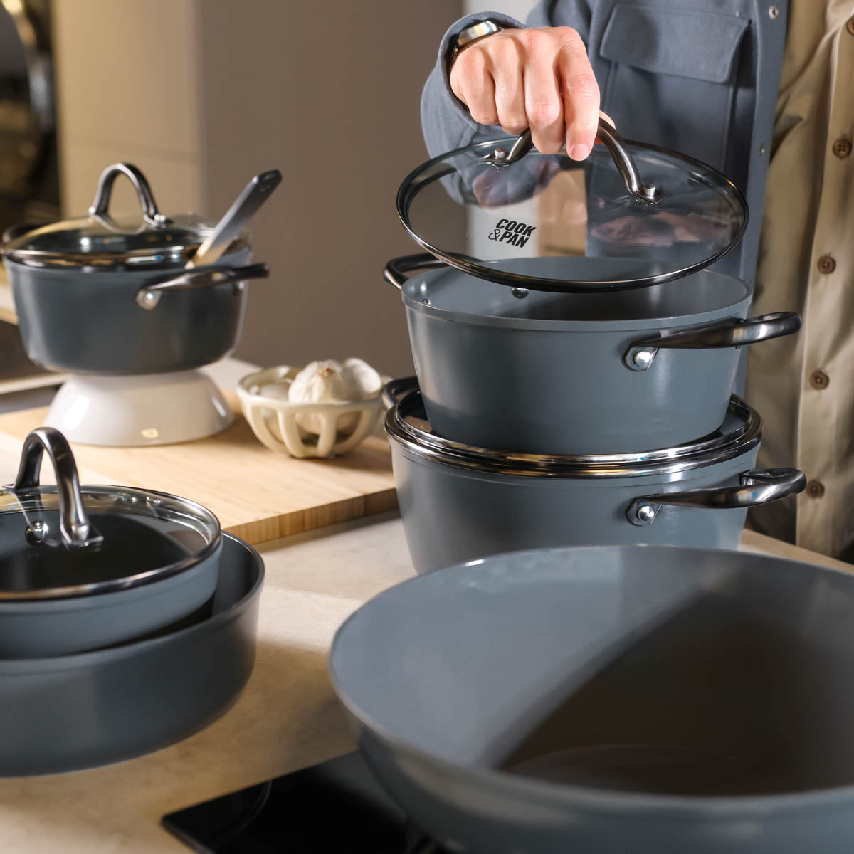 Grijze wokpan van 30 cm met glazen deksel en zwarte handvatten, mat afgewerkt.