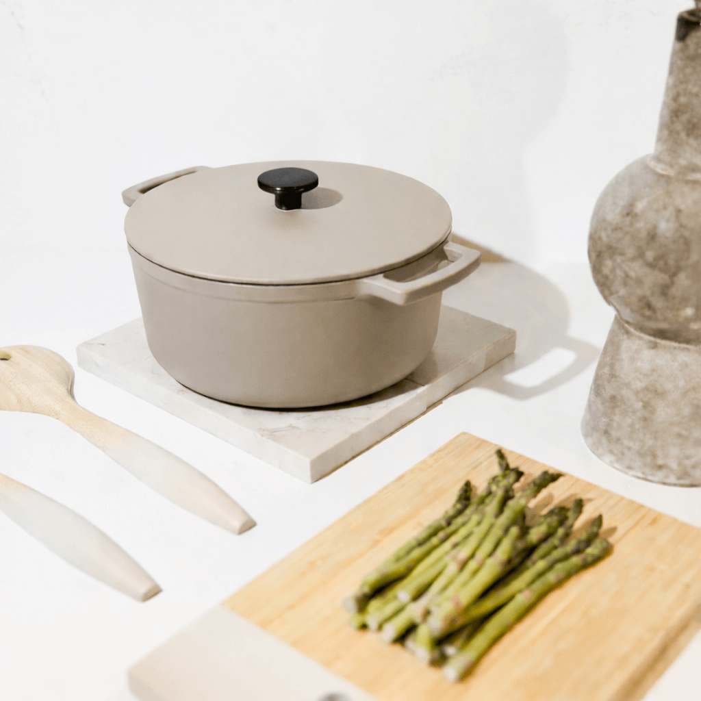 Cocotte en fonte taupe de 28 cm avec couvercle et poignées, posée sur une planche en marbre.