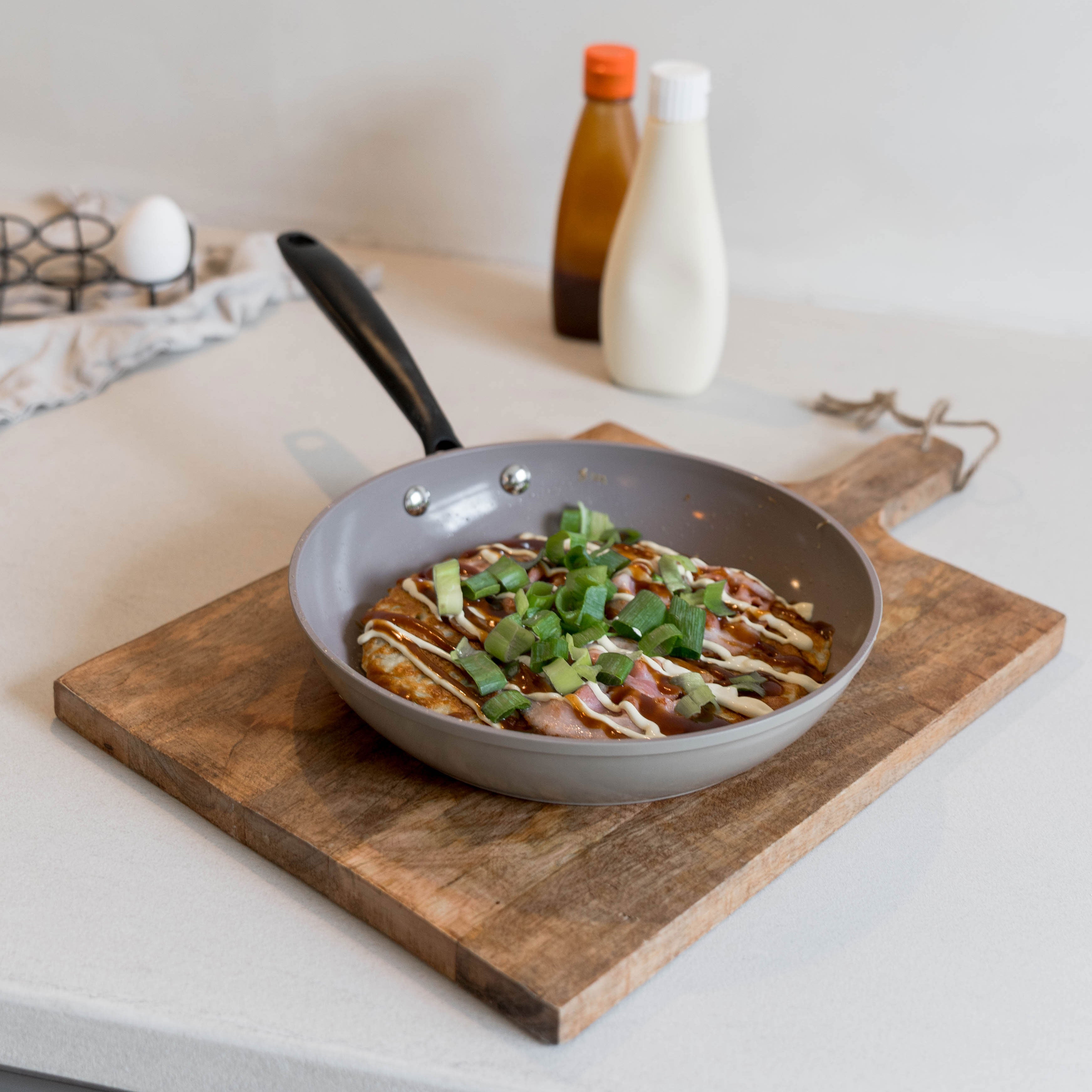 Taupe koekenpan met zwarte handgreep, gevuld met een gerecht en groene kruiden.