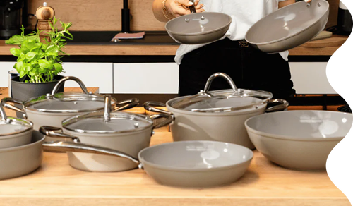 Taupe ceramic 12-piece cookware set with stainless steel handles and glass lids.