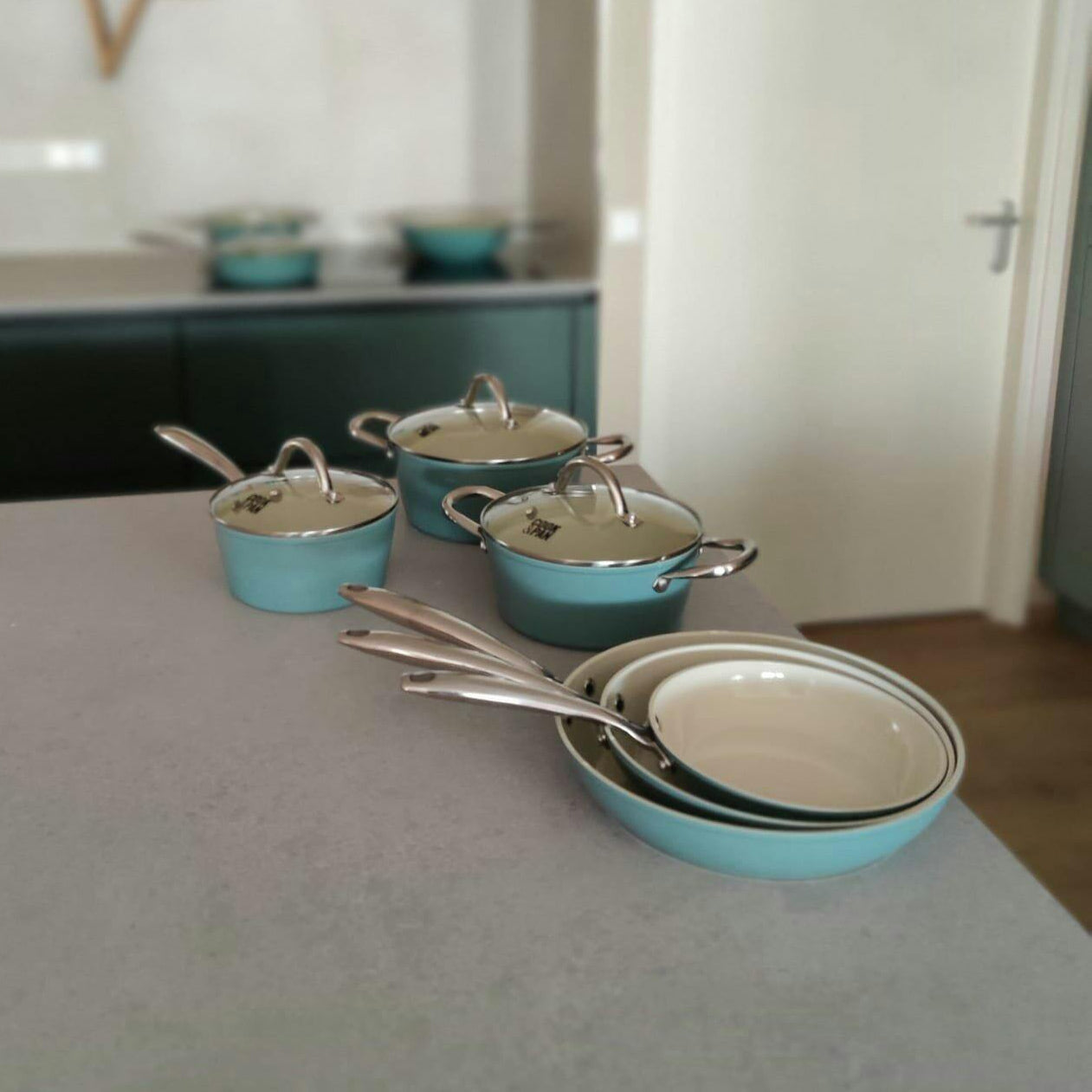 Batterie de cuisine bleu clair neuf pièces avec couvercles en verre et poignées argentées, casseroles pliables.