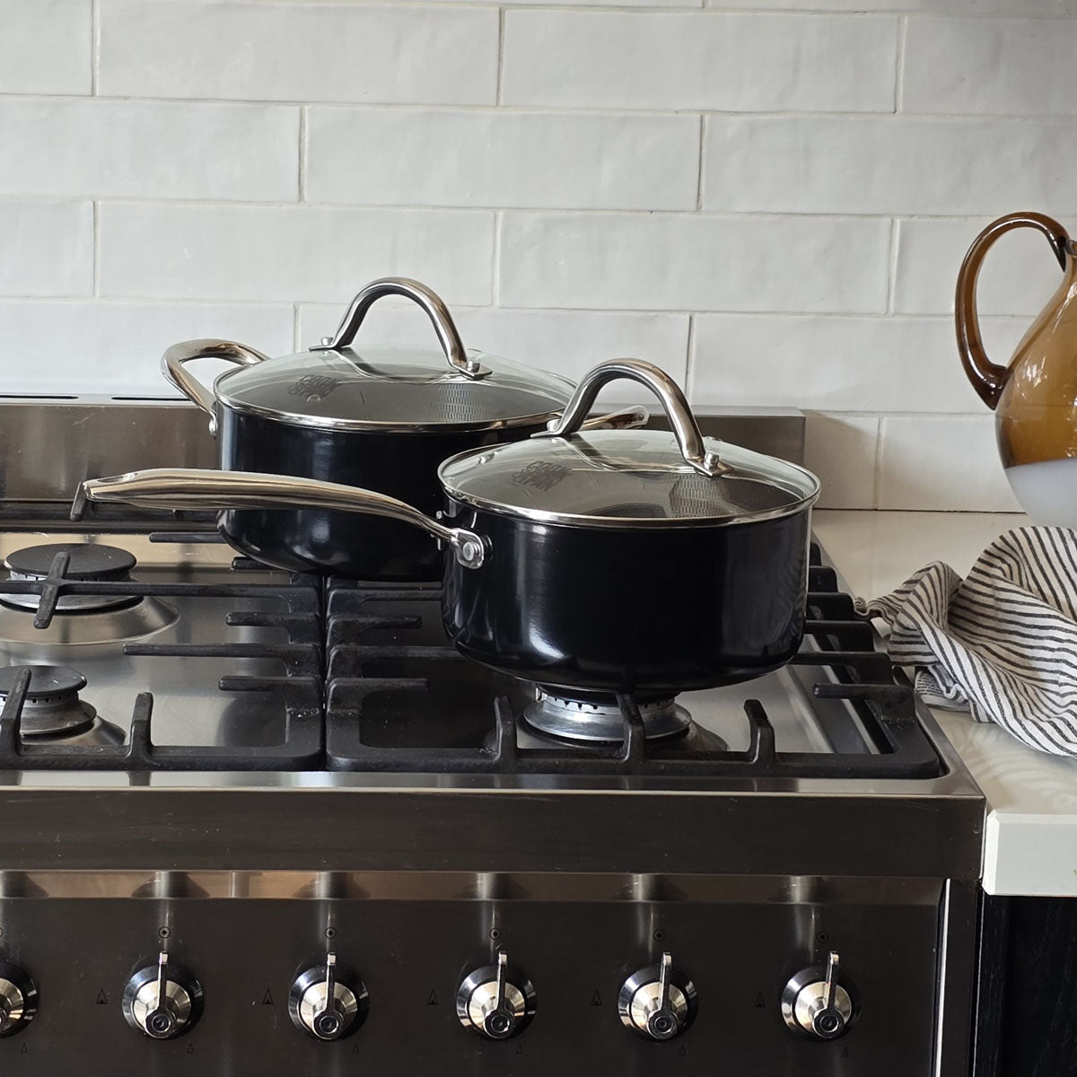 Batterie de cuisine noire avec poignées en acier inoxydable et couvercles en verre sur cuisinière à gaz.