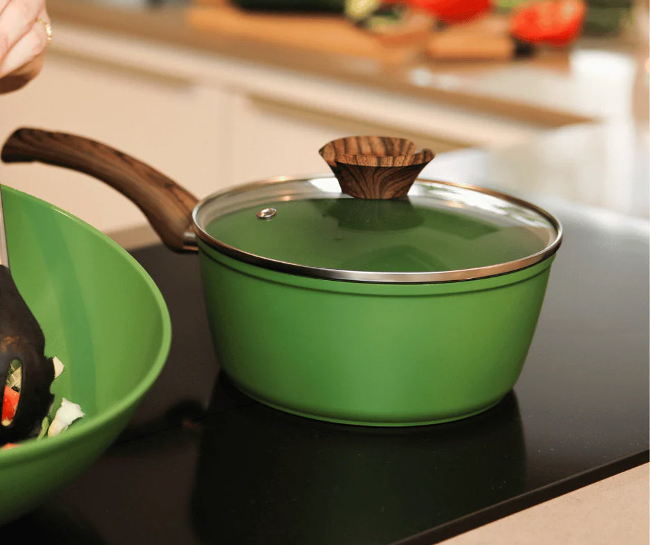 Grüne Sauteuse mit Glasdeckel und Holzoptikgriff auf schwarzem Kochfeld.