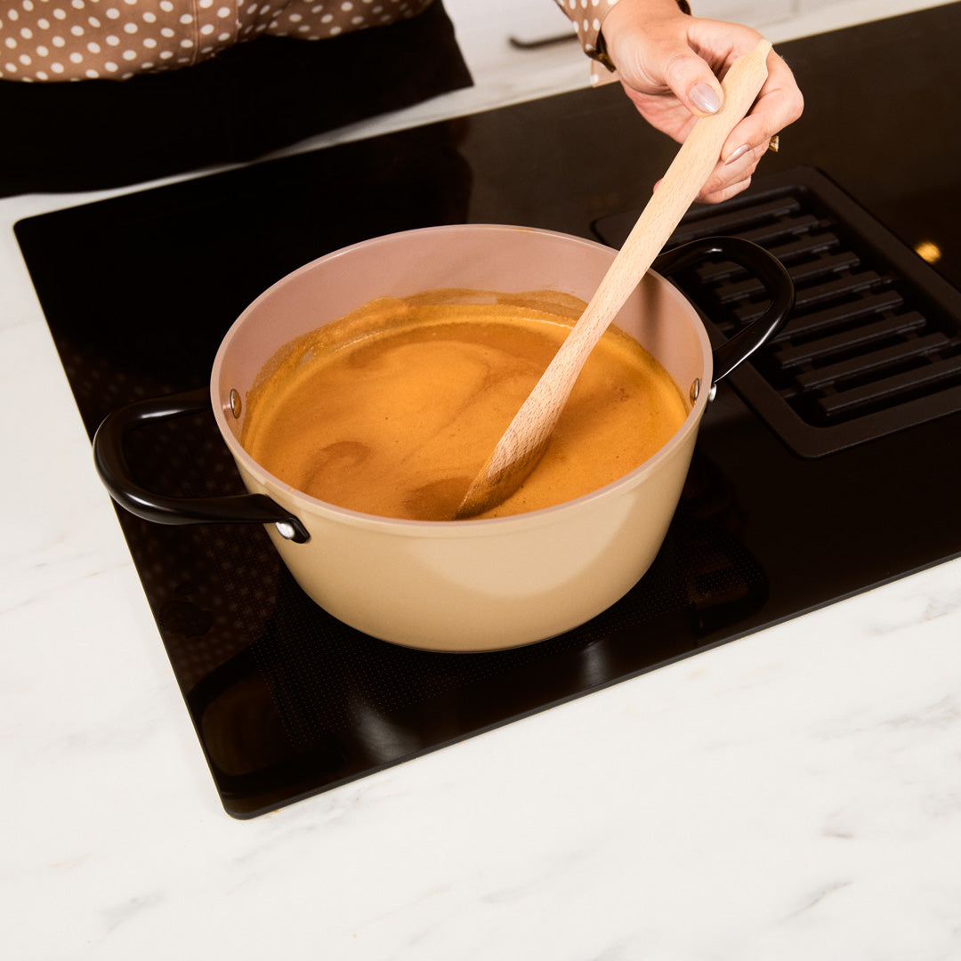 Taupe-colored 9-piece cookware set with wooden spoon on black induction cooktop.