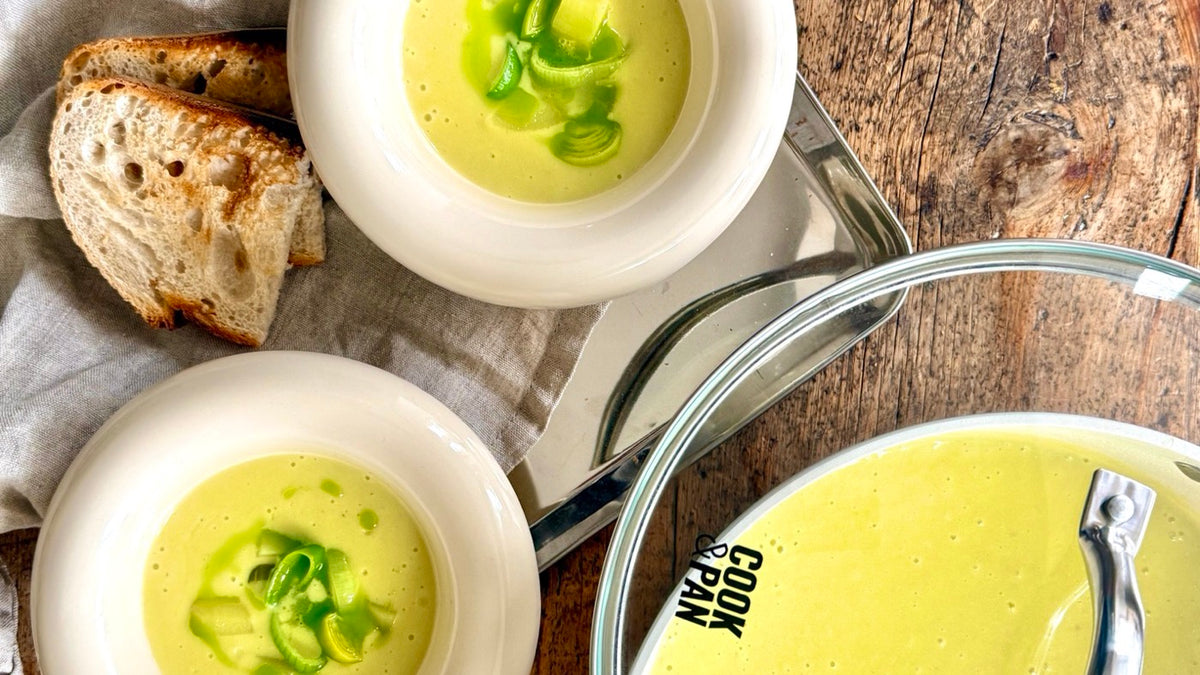 Twee kommen aardappel-preisoep met daslookolie, geroosterd brood en een Cook & Pan kookpan
