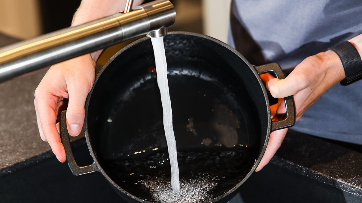 Water stroomt uit de kraan in een zwarte pan