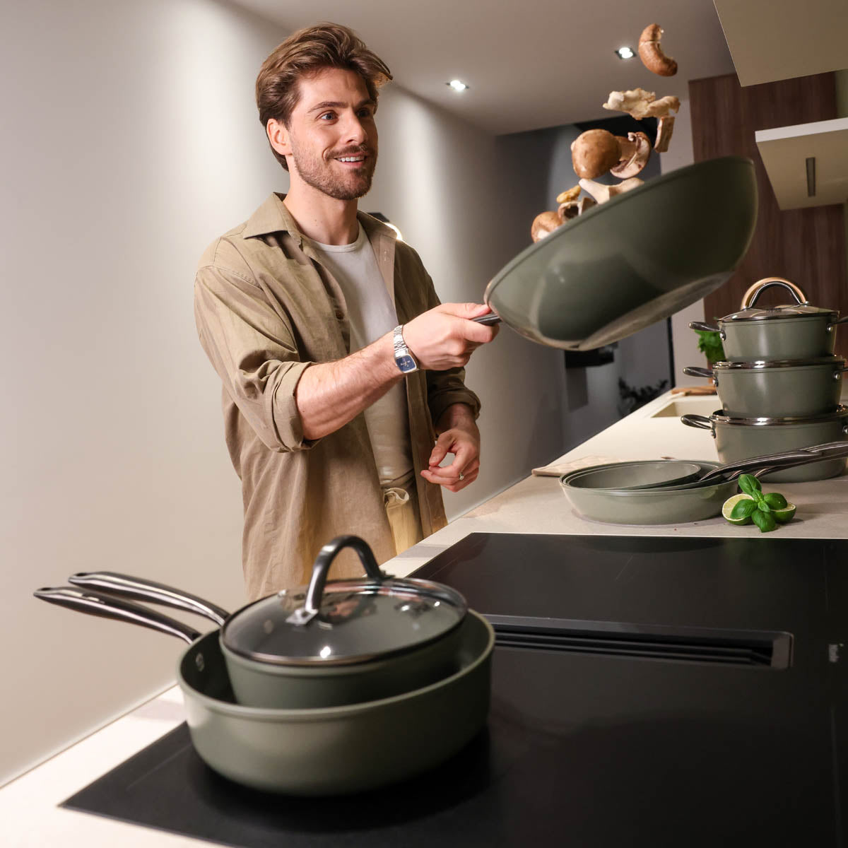Batterie de cuisine 9 pièces vert foncé avec couvercle en verre et poignées en acier inoxydable à côté d'une plaque de cuisson à induction.