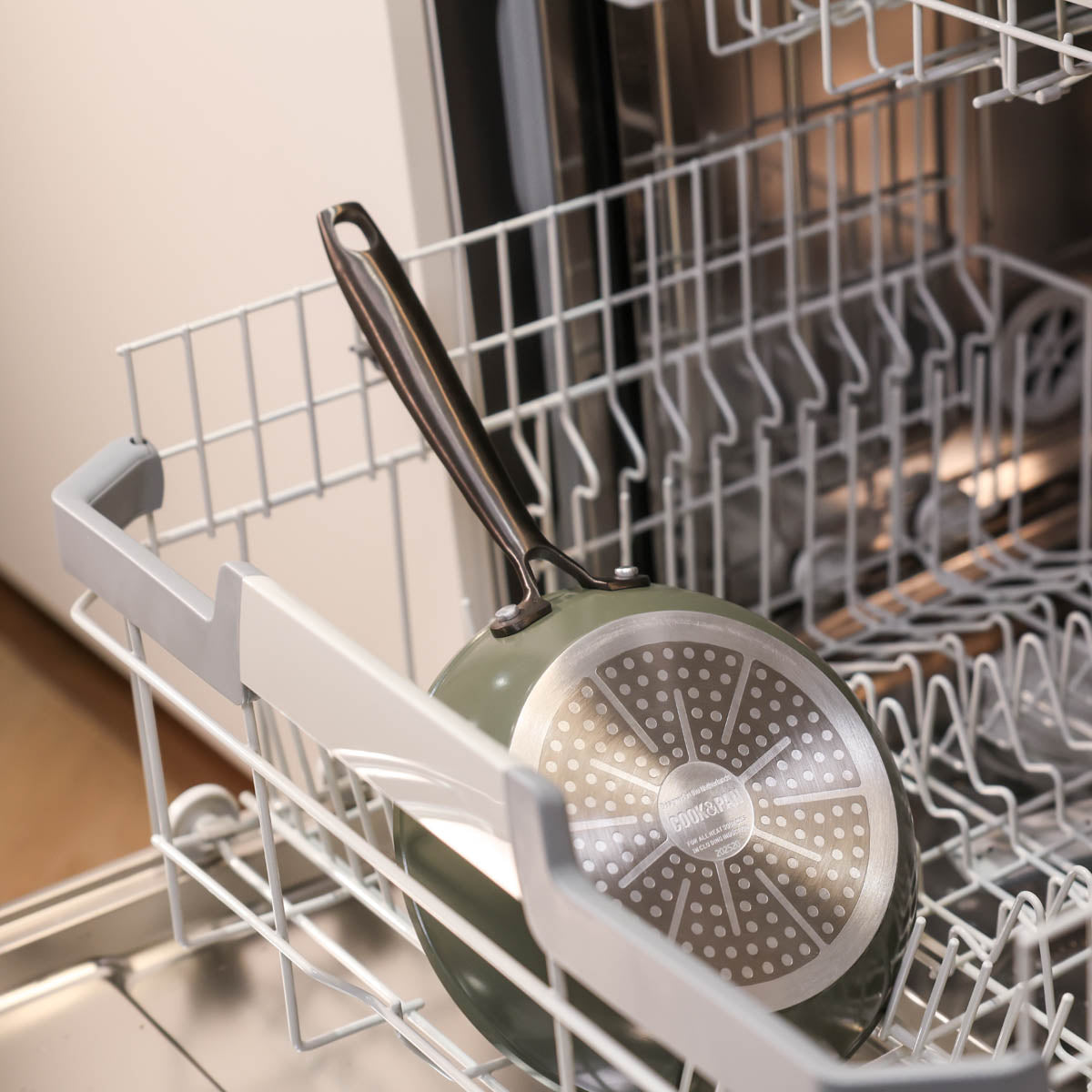 Casserole vert foncé avec fond en acier inoxydable placée dans le lave-vaisselle.