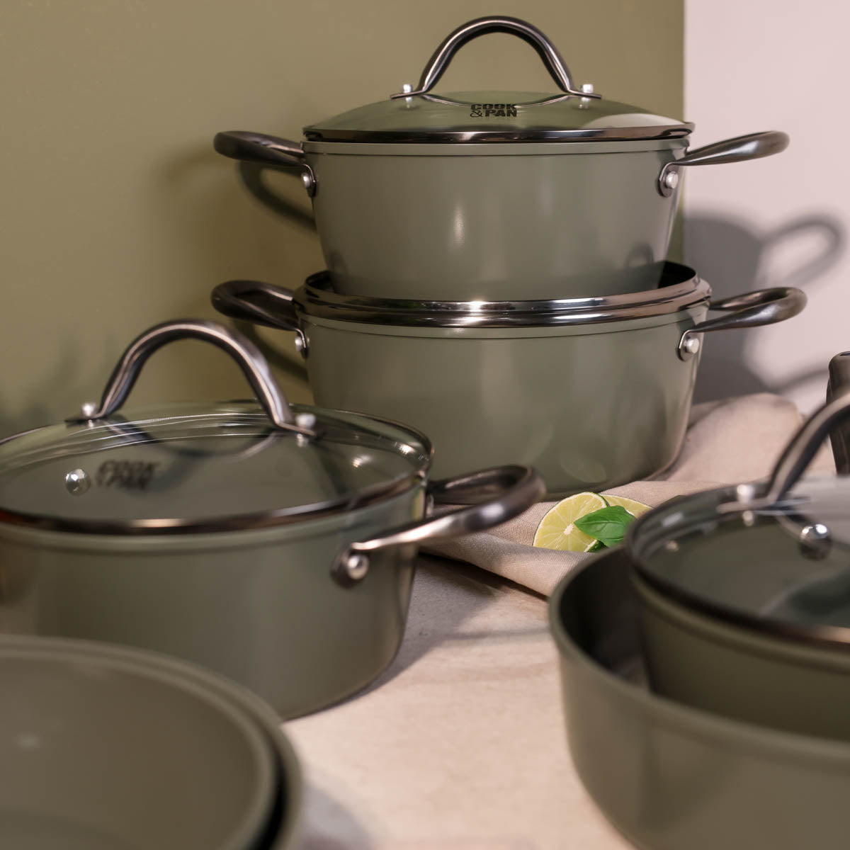 Batterie de cuisine 9 pièces vert foncé avec couvercles en verre et poignées en acier inoxydable.