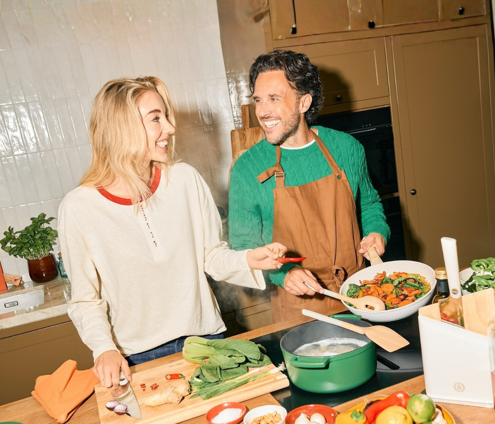 Zwei Personen kochen zusammen in einer Küche mit grünem Kochtopf auf dem Herd.