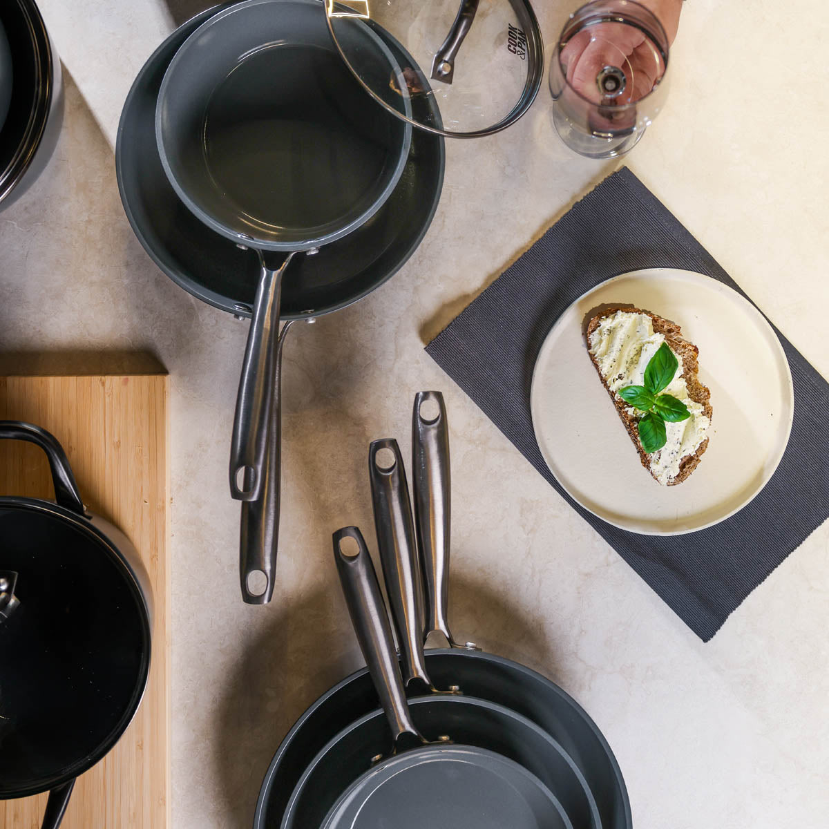 Black frying pan 24 cm with long handle, next to lid with glass rim and black pan rest.