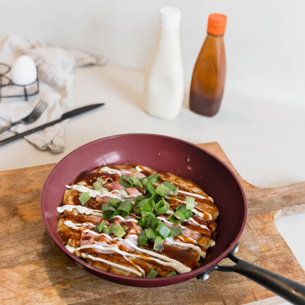 Cherry frying pan with okonomiyaki on a wooden board