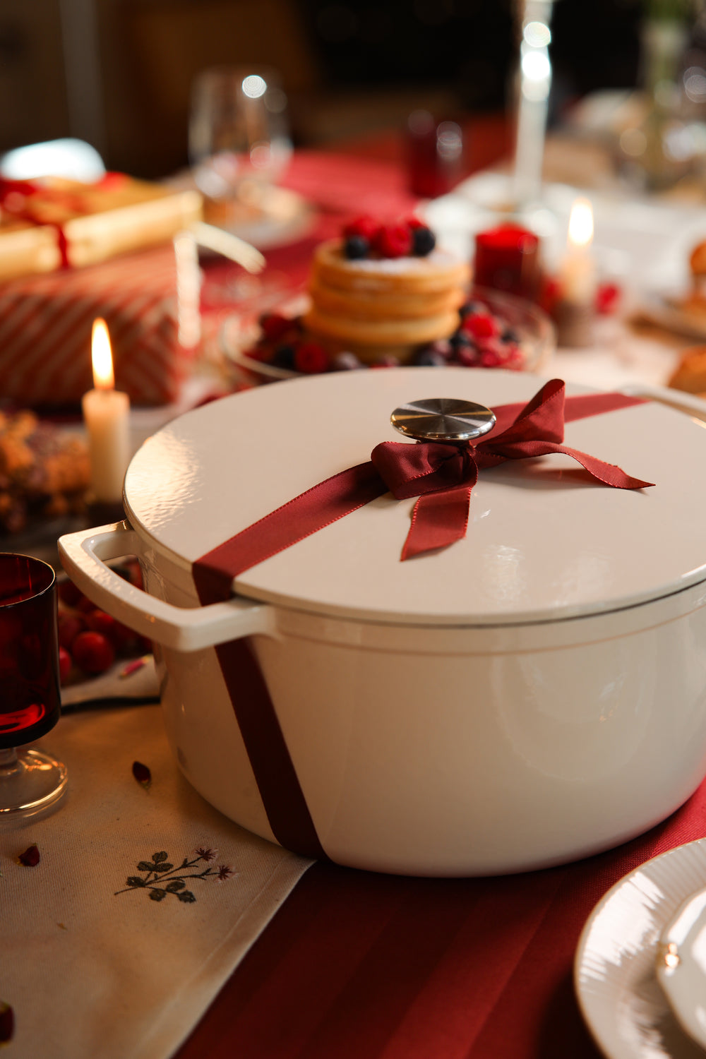 Weißer gusseiserner Bräter mit roter Schleife auf einem gedeckten Weihnachtstisch