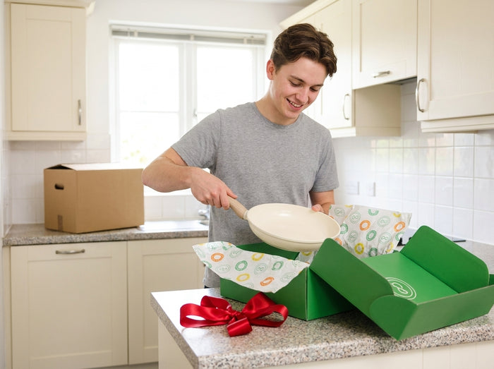 Un jeune habitant sort une poêle crème d'une boîte Cook & Pan verte avec papier de soie et nœud rouge