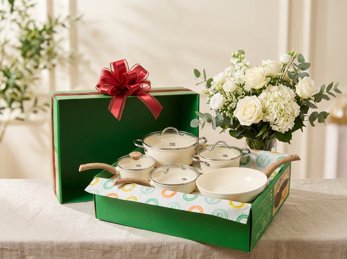 Boîte Cook & Pan verte ouverte avec nœud rouge et une batterie de cuisine crème sur une table de mariage aux fleurs blanches