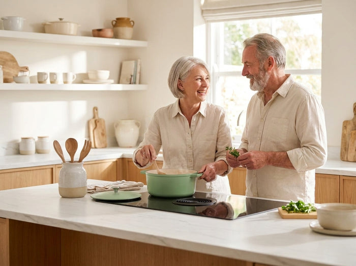 Un couple d'une soixantaine d'années cuisine ensemble avec une cocotte en fonte verte dans une cuisine claire