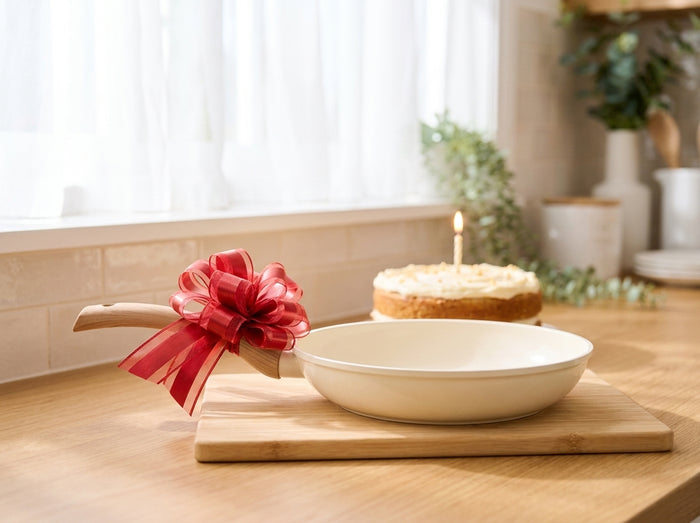 Poêle crème avec un nœud rouge sur une planche en bois, un gâteau et sa bougie en arrière-plan