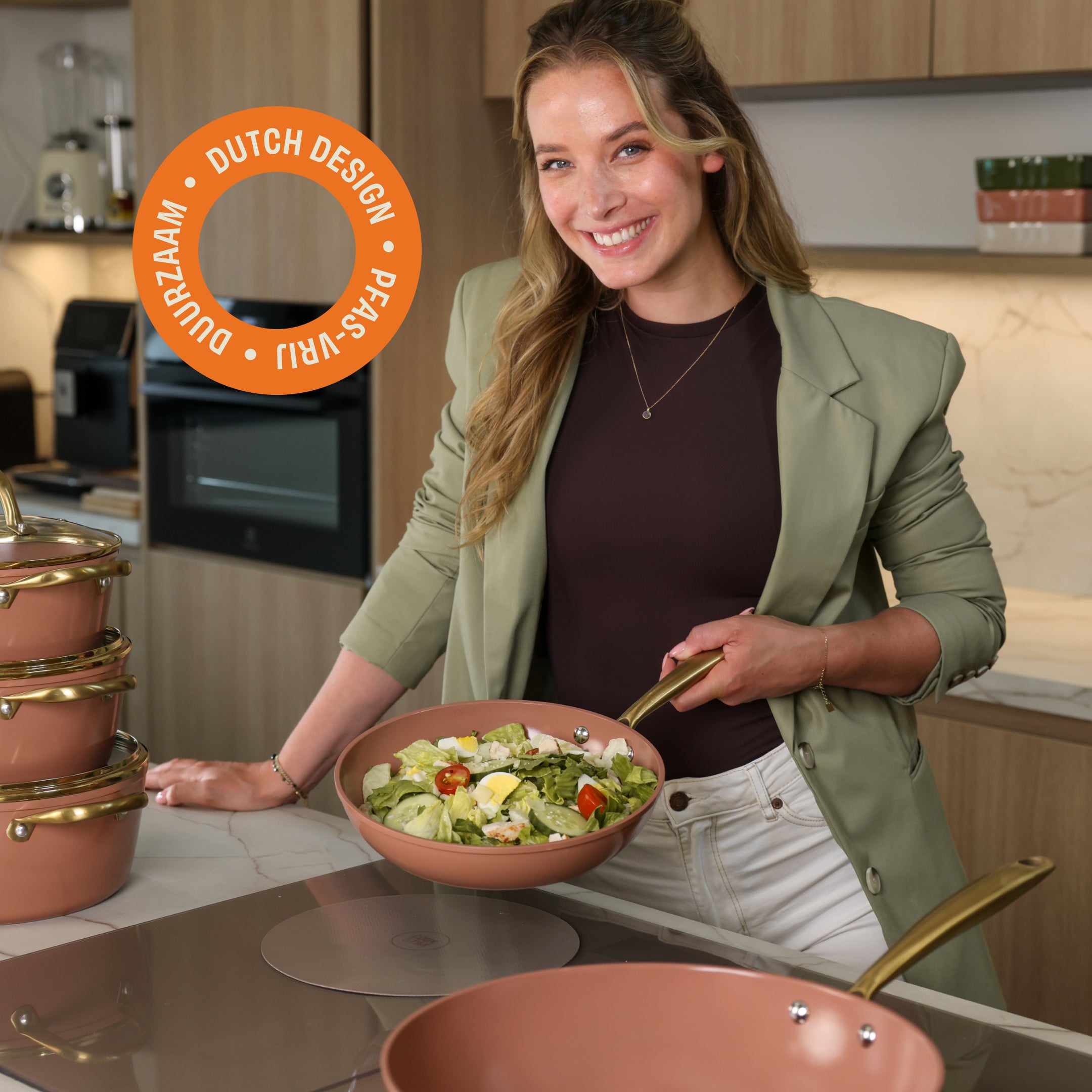 Vrouw in keuken met Sienna koekenpan gevuld met salade, omringd door bijpassende pannen met gouden handvatten
